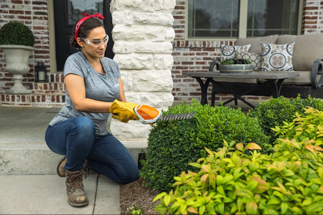 Woman pruning bush with Stihl outdoor equipment