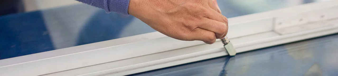 A close-up of a hand using a special tool and straight edge to cut glass