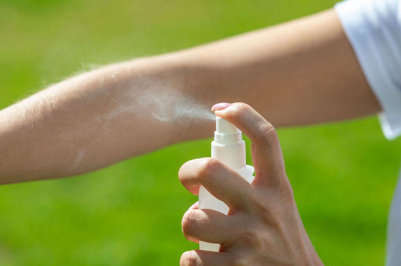 A person spraying their arm with mosquito repellent