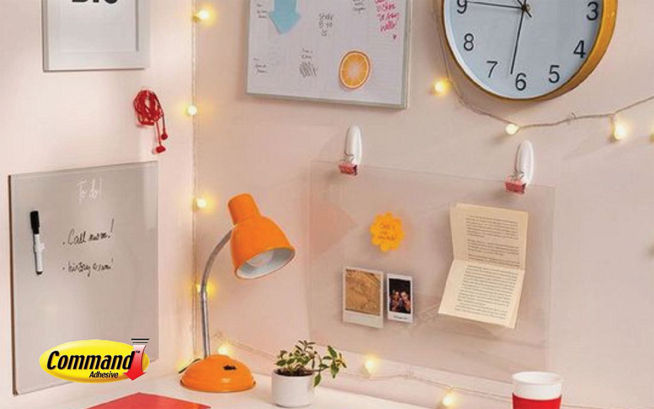 Top of dorm room desk with light pink walls and an orange lamp with string lights