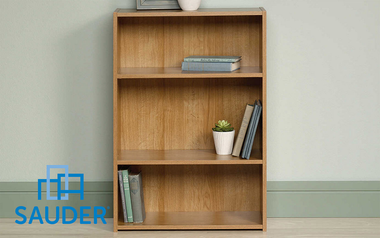 Sauder three shelf agaqinst a wall with a few books and plants on the shelves