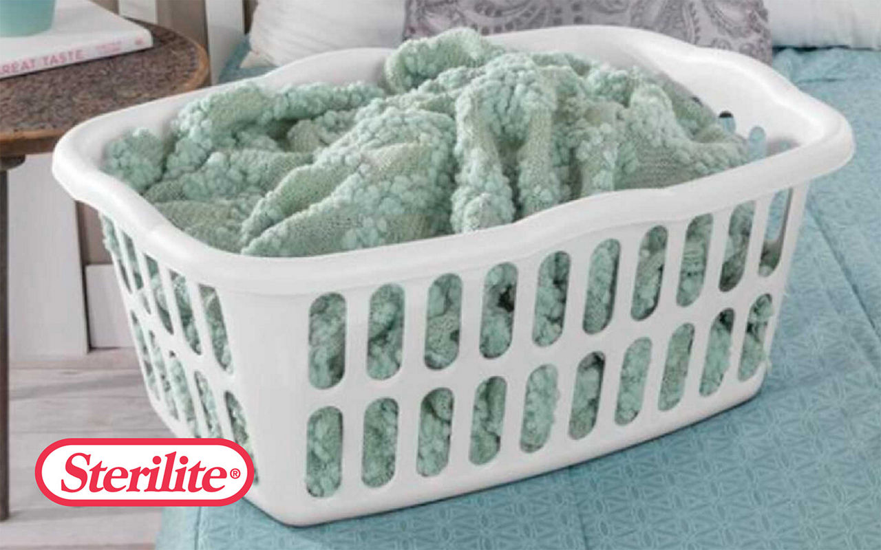 Sterilite laundry basket with a blue green blanket on top of a bed