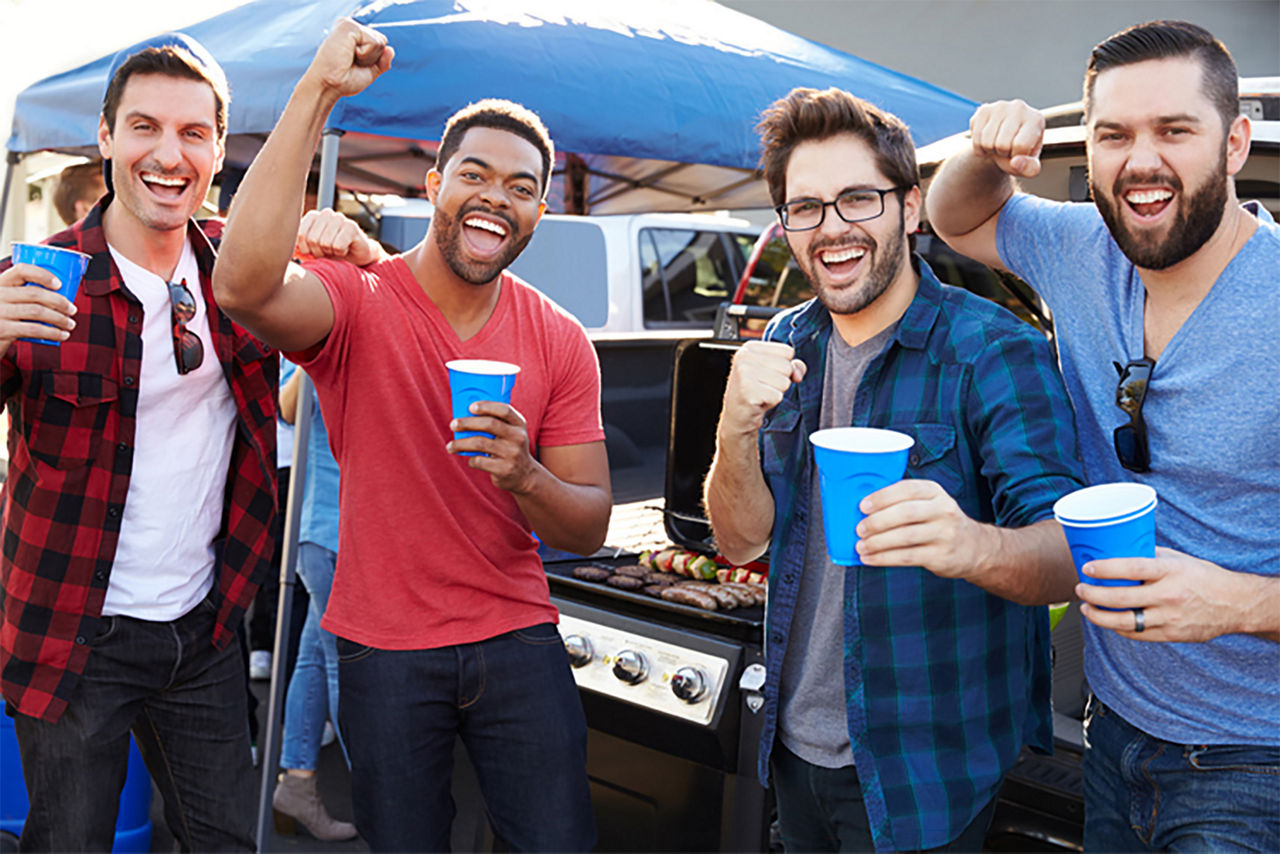 4 men tailgating with cups in their hands and cheering