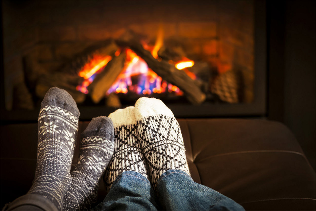 Two people wearing holiday socks with their feet by a fireplace