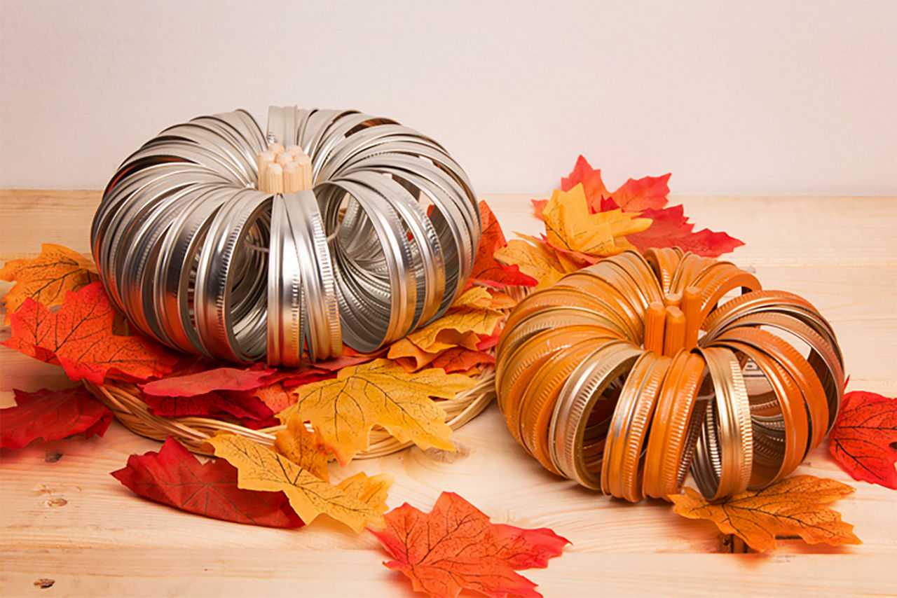 Finished prodcut of mason jar lid pumpkins painted and non-painted on a bed of leaves