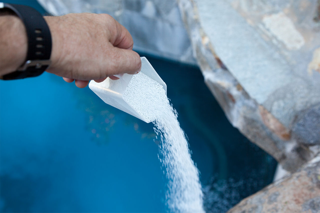 Pouring chlorine into swimming pool as part of a regular maintenance.