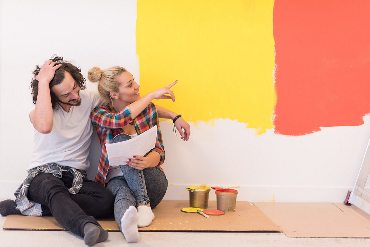 Two people sitting on the floor deciding if the wall looks better in yellow or red