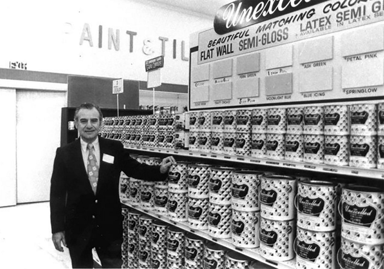 Old black and white photo of a guy in front of the Valu paint aisles