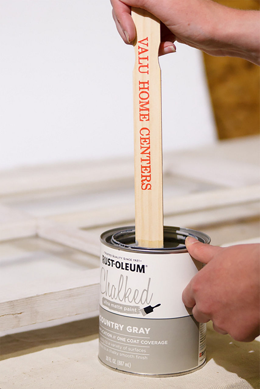 A Valu Home Center paint stirrer stick inside a can of rust-oleum gray paint