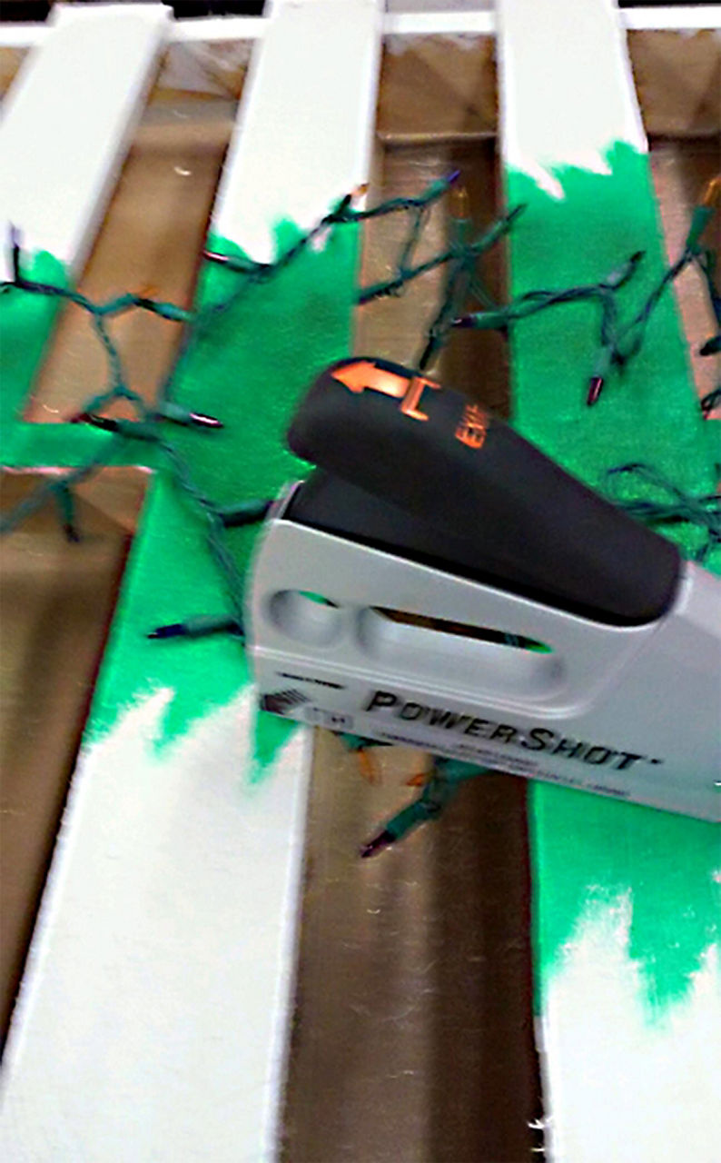 Staple gun getting ready to staple the christmas tree string lights onto the pallet