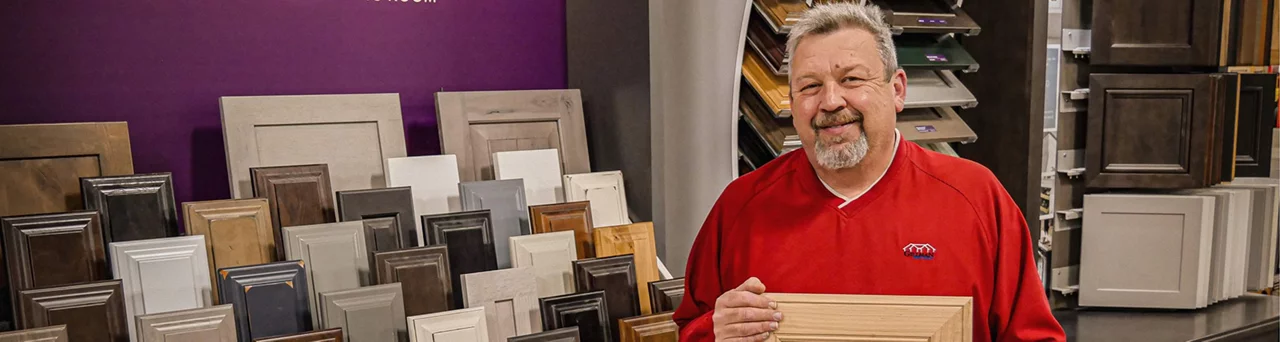 A man wearing a red shirt standing in front of a cabinet display holding a cabinet door