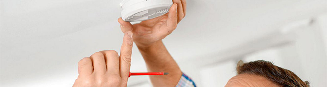 Man holding a screwdriver in one hand as he fixes smoke alarm cover