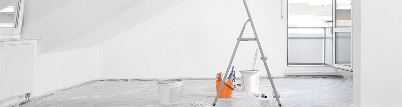 Room being painted white with plastic drop cloth, a ladder in the middle of the room and buckets