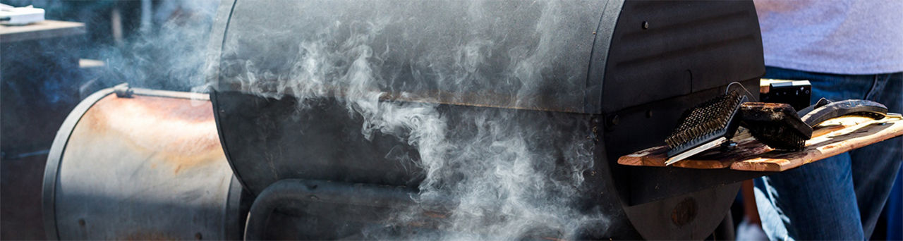 Black pellet grill with smoke rolling out of it as it is cooking food