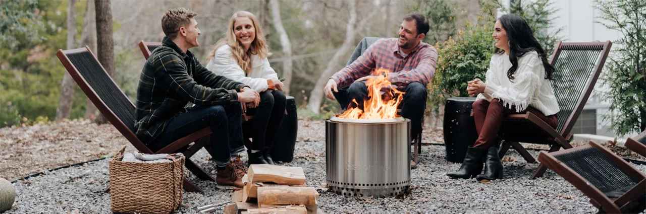Four people sitting around a Solo Stove in the woods 