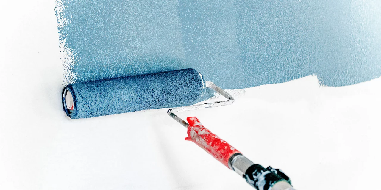 Painting a white wall with a paint roller with blue paint on it 