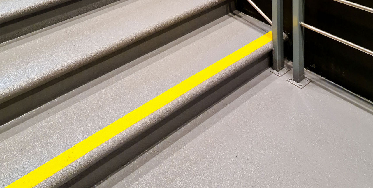 yellow warning sign on stairs signifying a potential hazard, steep stairs and care to be taken when going up or down stairs