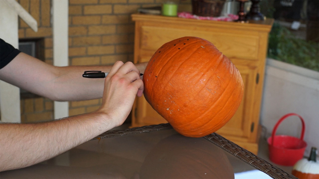 Person sketching with a sharpie where they will drill their pumpkin