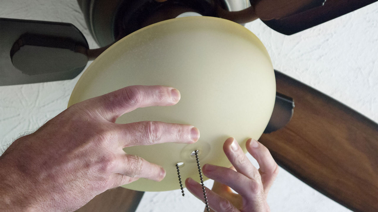 A person attaching a light to a ceiling fan light