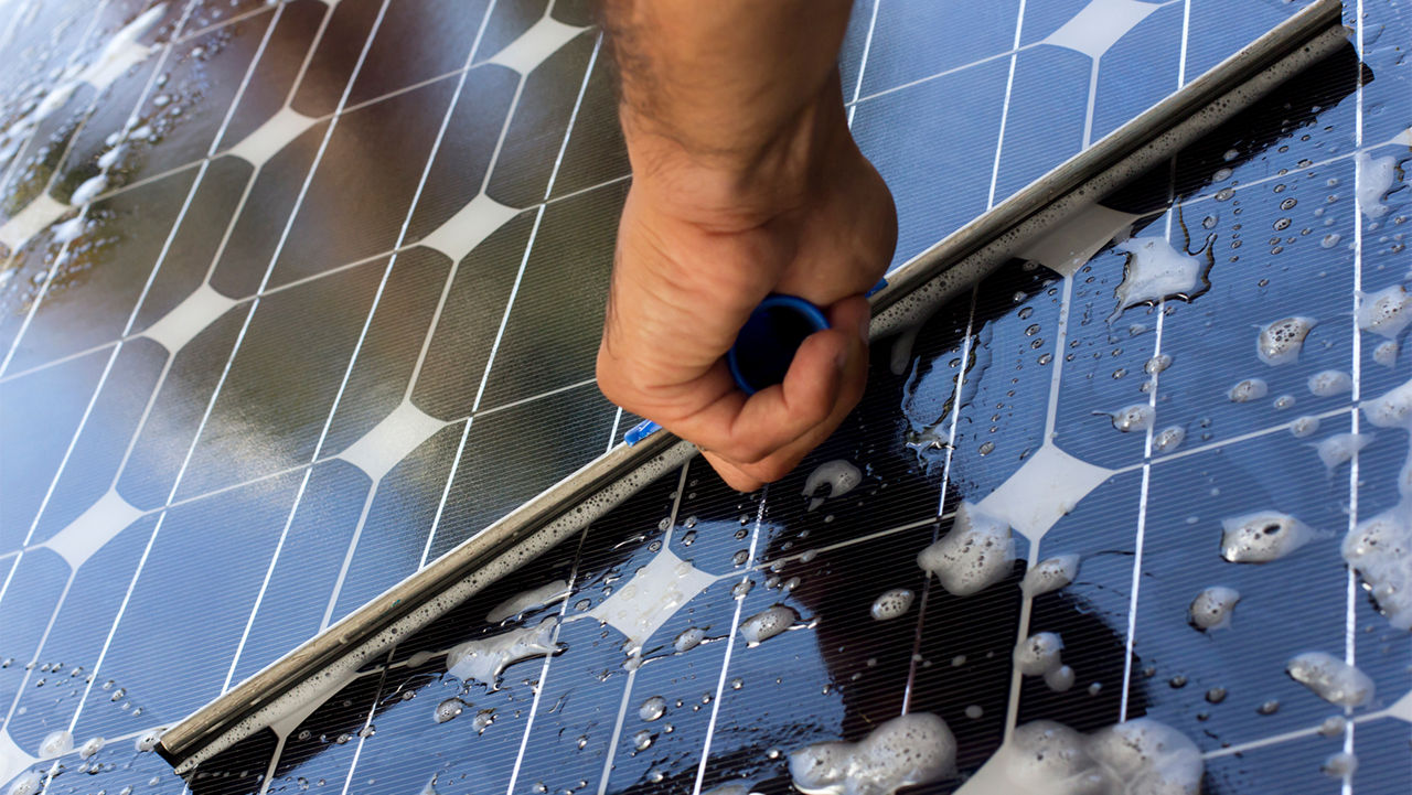 Hand cleaning a solar panel with a squeegee