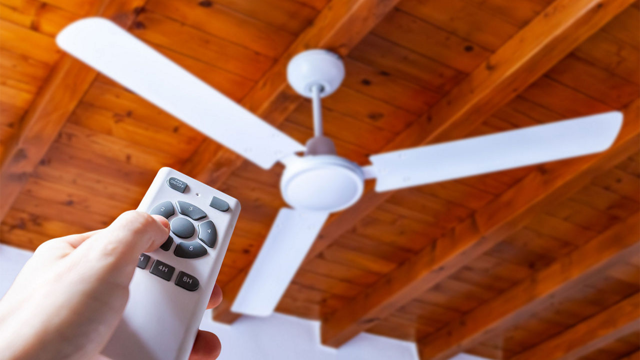 A person turning on a ceiling fan with a remote 