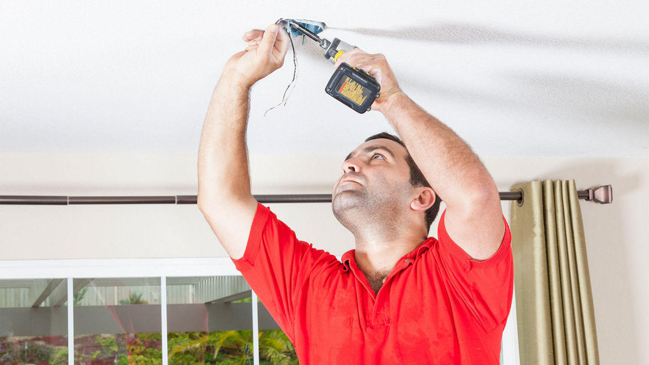 A man installing a ceiling fan bracket
