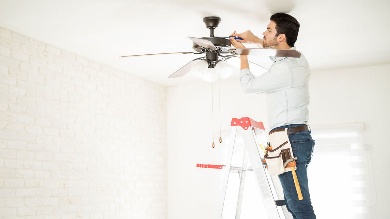 A man standing on a ladder installing a ceiling fan