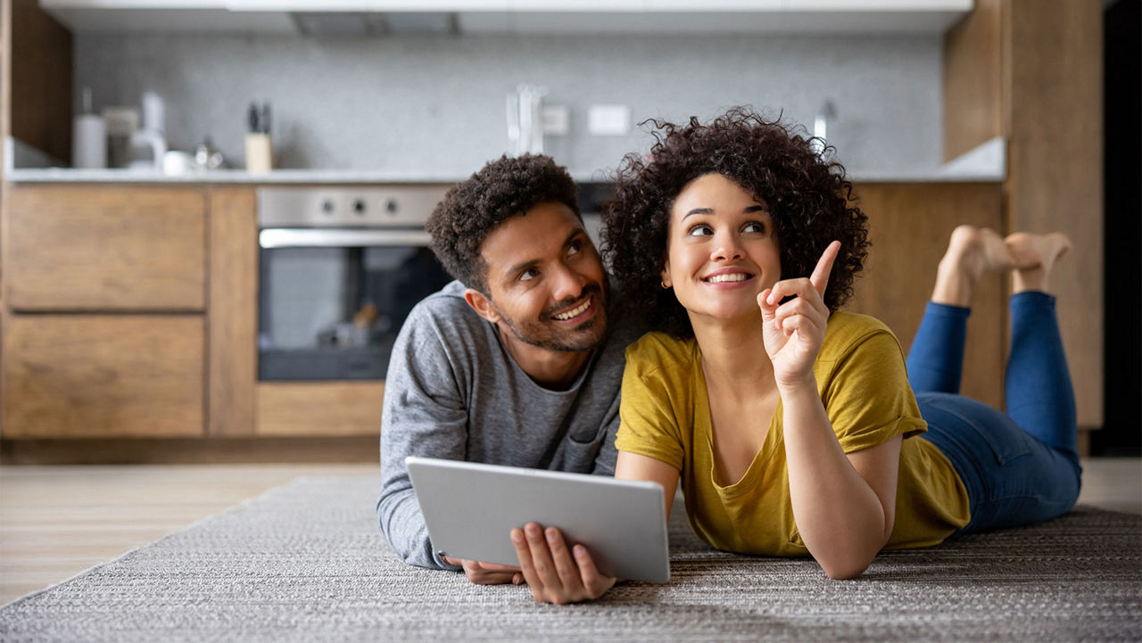 A couple laying on the floor with a tablet discussing design plans for their kitchen