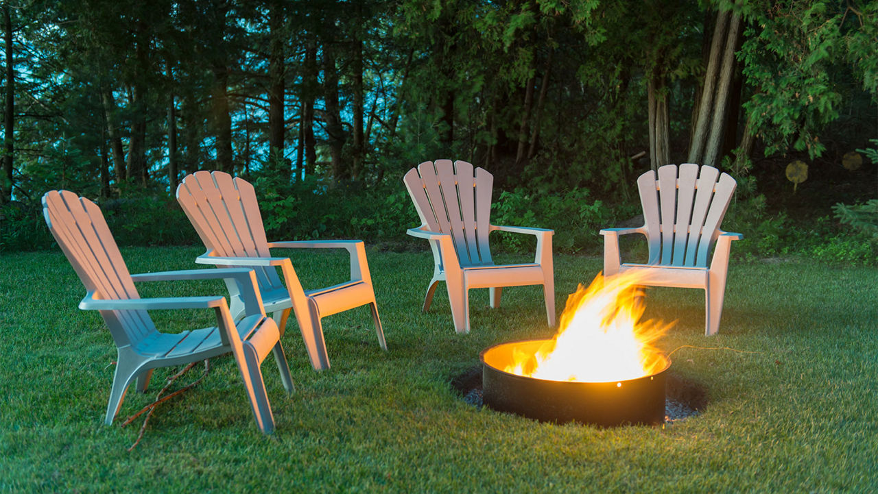 A fire pit sitting in a yard with white chairs around it 