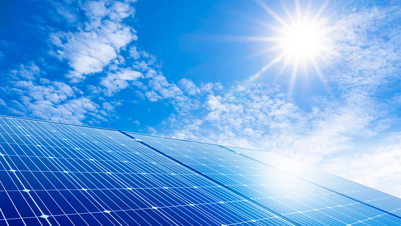 Blue sky and the sun shining down upon solar panels 