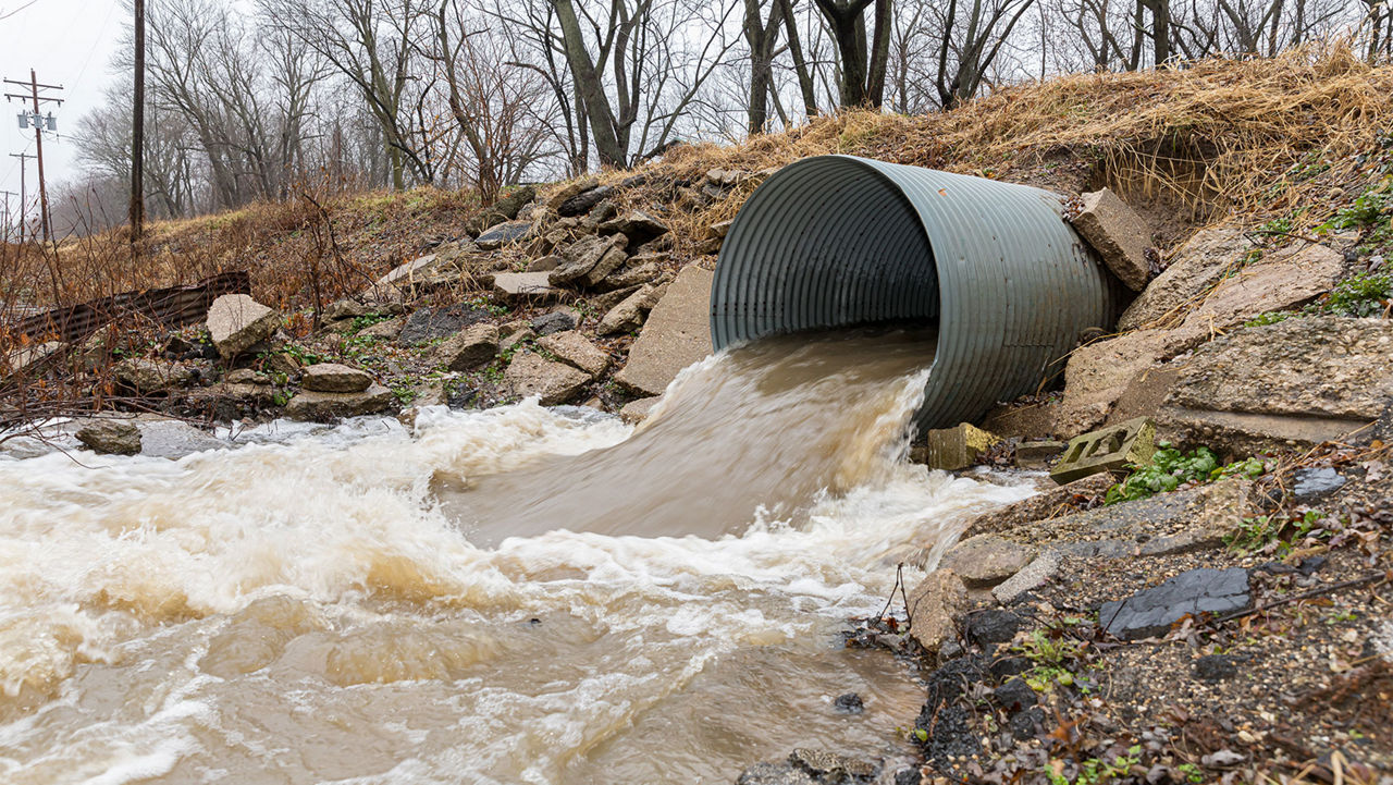 Closeup motion blur of storm water runoff flowing through metal drainage culver under road. January storms brought heavy rain and flash flooding to Illinois