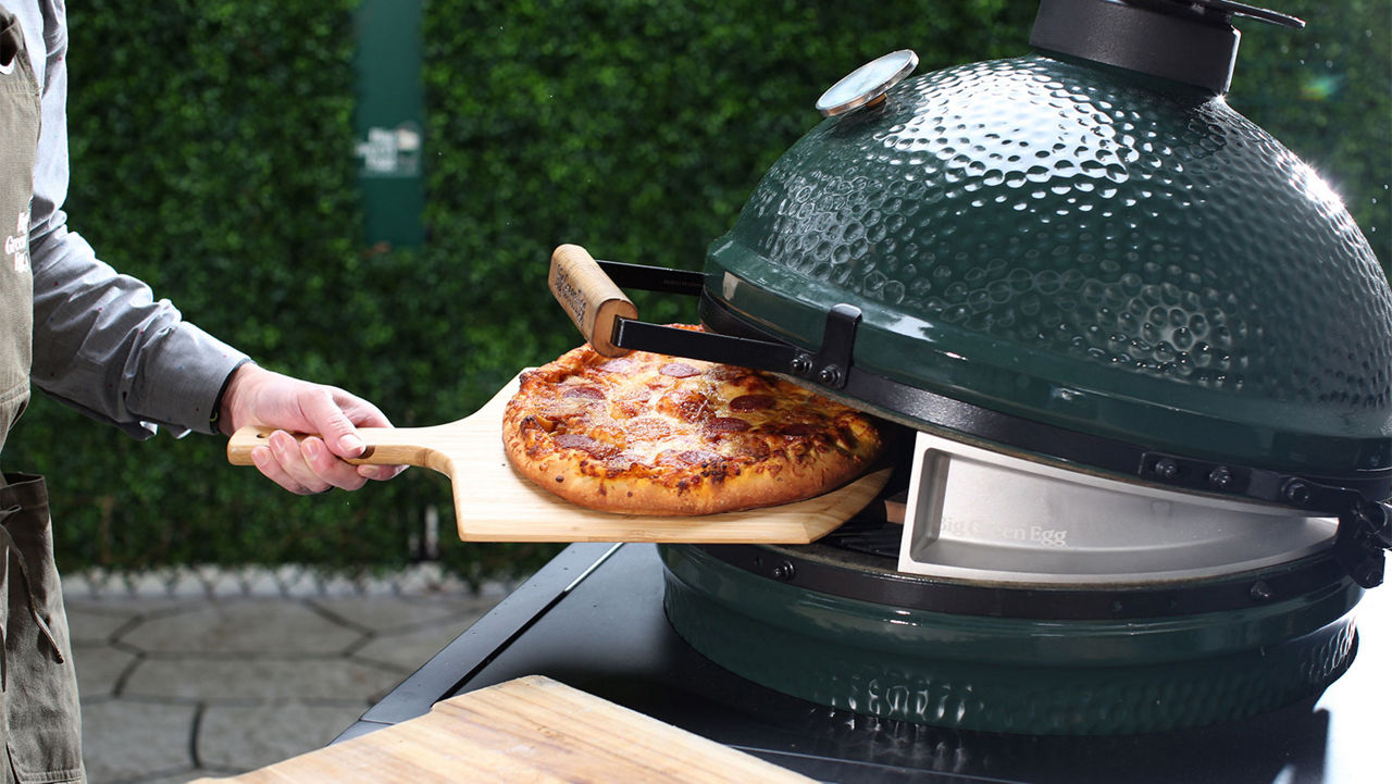 A man putting a pizza in a Big Green Egg