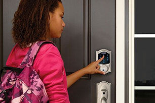 Girl with pink backpack punching in code to Schlage keyless deadbolt on front door