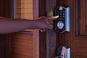 Person punching in code to Schlage keyless deadbolt on front door in the dark