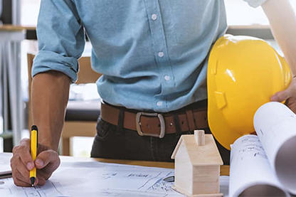 Contractor holding a yellow hard hat on his hip while drawing on a planning sheet