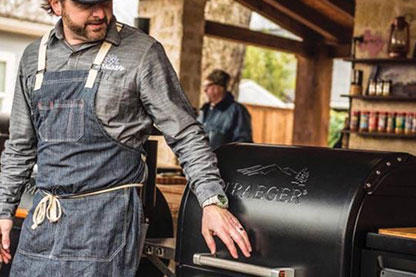 Man wearing grilling apron standing next to his Traeger
