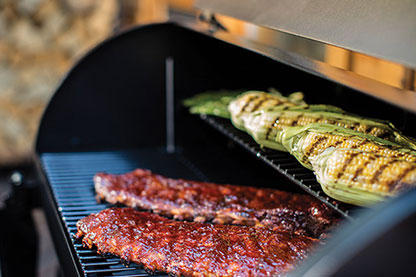 Rack of ribs and grilled corn cooking on a Traeger grill