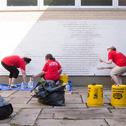 Valu Crew volunteers painting a portion of a brick wall white for a mural