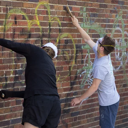 Participants scrubbing graffitied brick wall with wire brushes