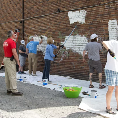 Participants using paint rollers and brushes to put paint on the brick wall outside of CoLab