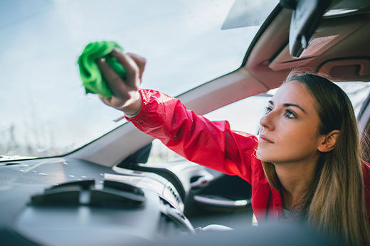 A woman wiping the inside-front windshield of a vehicle with a green cloth.