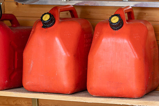 Two red gas cans sitting on a wood shelf