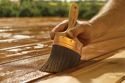 man using a paint brush to stain a deck