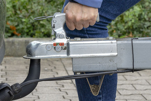 A man setting up a metal trailer hitch to a truck.