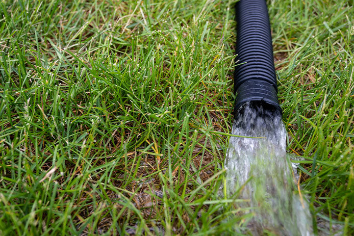 Draining water out of a black drainpipe into grass