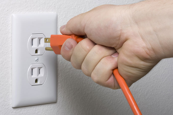 Person pulling the plug of an extension cord from an electrical outlet