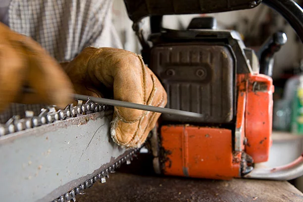 Man wearing leather work gloves sharpening a chainsaw blade