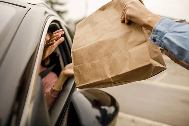 Employee handing a woman in her car a brown paper bag 