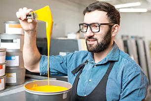 A man wearing glasses and an apron mixing a custom paint color