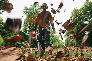 Man wearing safety glasses and ear protection using an ECHO blower to clear leaves